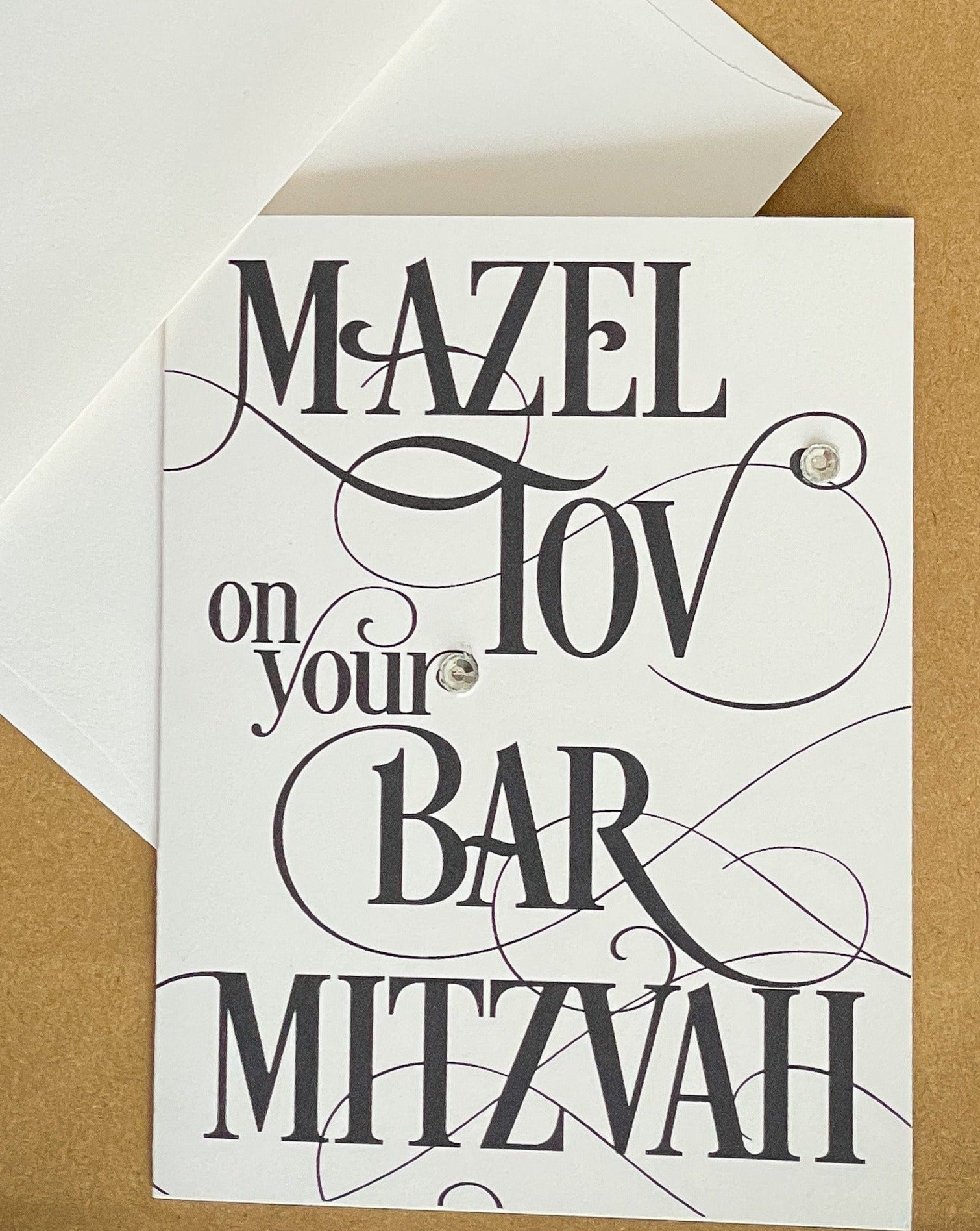 this is a note card on a craft paper gift bag with a white envelope and a black marker , the card says Mazel Tov on your bar mitzvah in a black script font