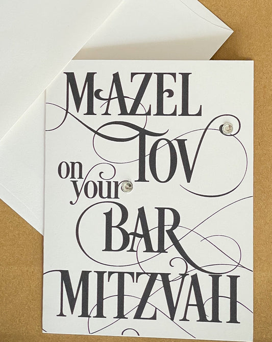 this is a note card on a craft paper gift bag with a white envelope and a black marker , the card says Mazel Tov on your bar mitzvah in a black script font
