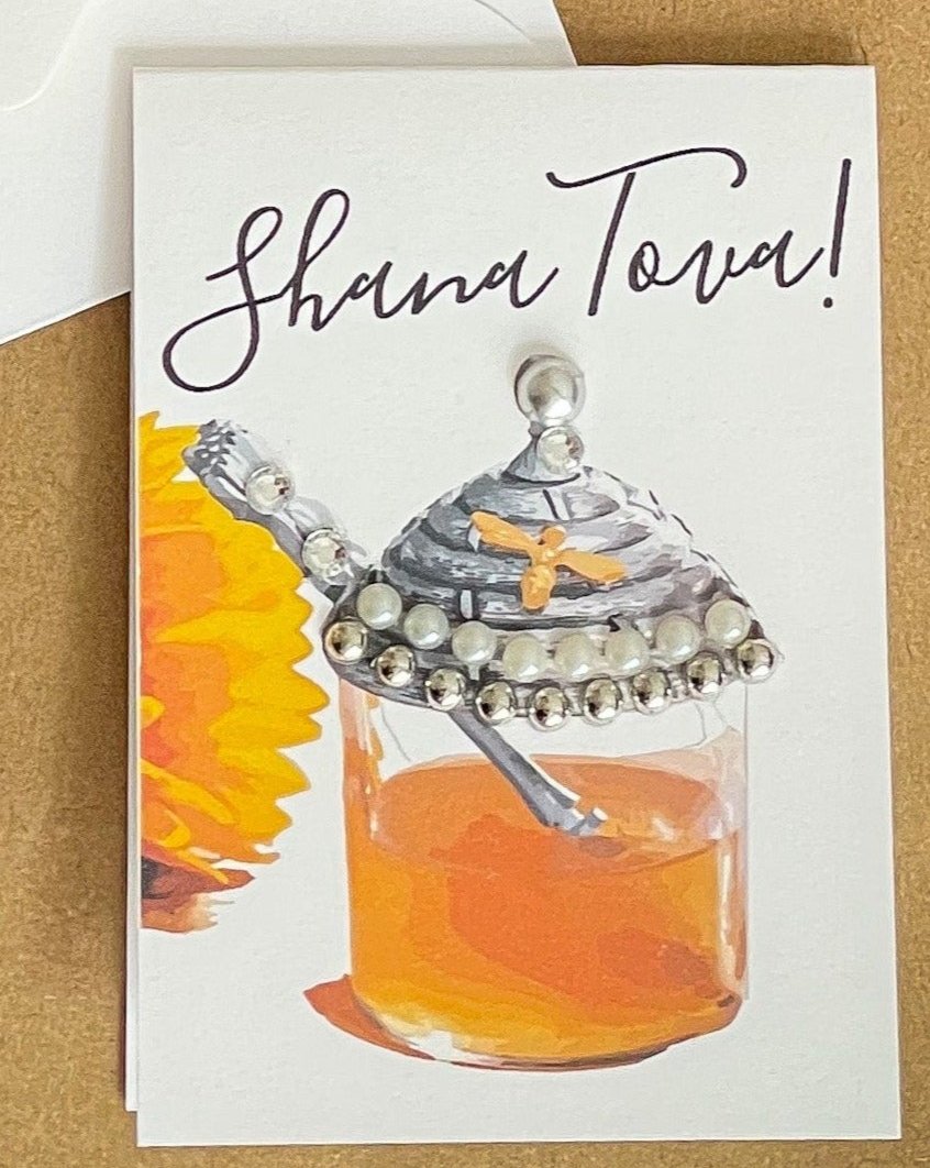 this is a mini note card on a craft paper gift bag with a white envelope and a black marker , the card says Shana Tova in English with a glass jar of honey 
