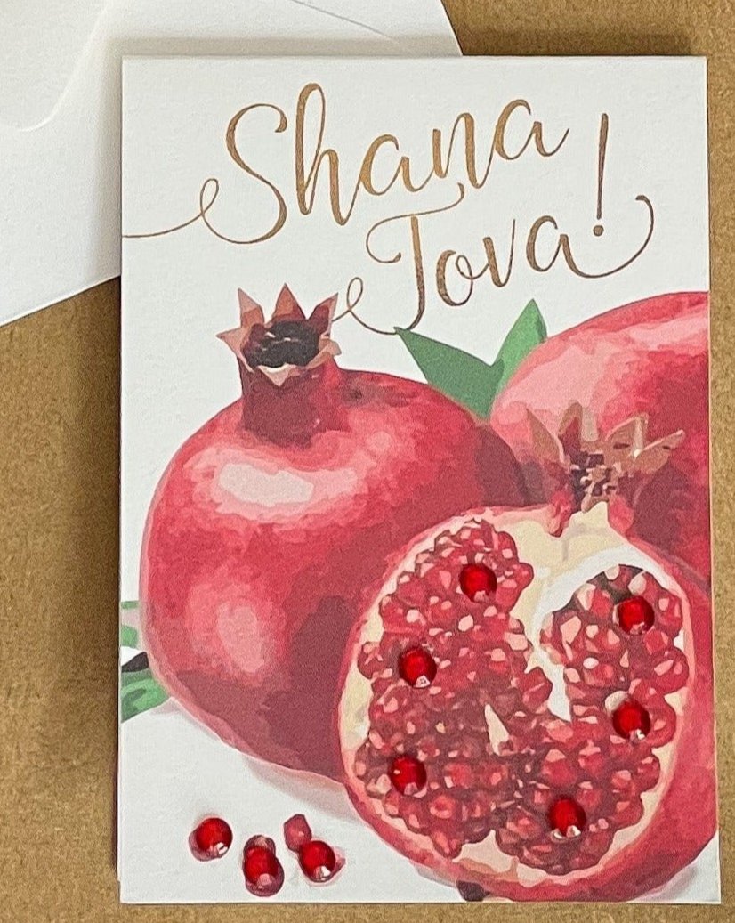 this is a mini note card on a craft paper gift bag with a white envelope and a black marker , the card says Shana Tova in English with a group of pomegranates